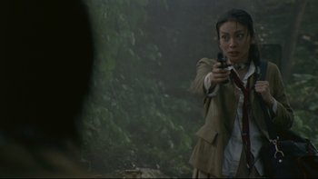 Movie still from “Battle Royale” (2000), directed by Kinji Fukasaku – A woman holding a gun while standing next to a tree; Close Up shot, Over the shoulder angle