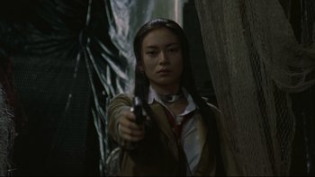 Movie still from “Battle Royale” (2000), directed by Kinji Fukasaku – A woman holding a gun while standing next to a tree; Medium shot, Low angle