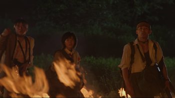 Movie still from “Battle Royale” (2000), directed by Kinji Fukasaku – A man and a woman standing in front of a fire; Medium shot, Low angle
