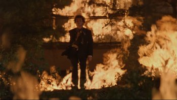 Movie still from “Battle Royale” (2000), directed by Kinji Fukasaku – A man standing in front of a fire; Wide shot, Low angle