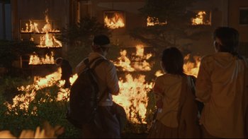 Movie still from “Battle Royale” (2000), directed by Kinji Fukasaku – A group of people standing in front of a burning building; Extreme Wide shot, Low angle