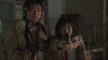 Movie still from “Battle Royale” (2000), directed by Kinji Fukasaku – A man and a woman holding guns in a room; Medium shot, Low angle
