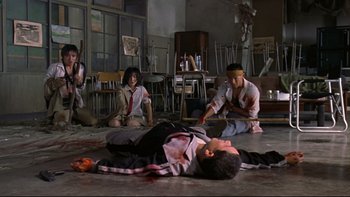 Movie still from “Battle Royale” (2000), directed by Kinji Fukasaku – A group of people sitting and standing in a room; Wide shot, High angle