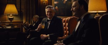 Movie still from “Battle of the Sexes” (2017), directed by Valerie Faris – A man in a suit and tie holding a glass; Medium shot, Over the shoulder angle