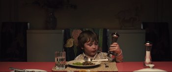 Movie still from “Battle of the Sexes” (2017), directed by Valerie Faris – A child sitting at a dinner table with a fork in his mouth; Medium shot, High angle