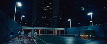 Movie still from “Battle of the Sexes” (2017), directed by Valerie Faris – Two people are playing tennis on a tennis court at night; Extreme Wide shot, Low angle
