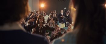 Movie still from “Battle of the Sexes” (2017), directed by Valerie Faris – A group of people taking pictures in a room; Medium shot, Over the shoulder angle