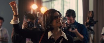 Movie still from “Battle of the Sexes” (2017), directed by Valerie Faris – A woman in a black shirt and some people taking pictures; Medium shot, Over the shoulder angle