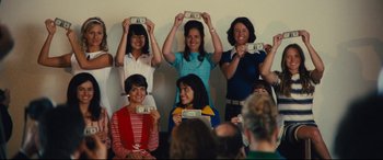Movie still from “Battle of the Sexes” (2017), directed by Valerie Faris – A group of women holding up money in front of their faces; Medium shot, Low angle