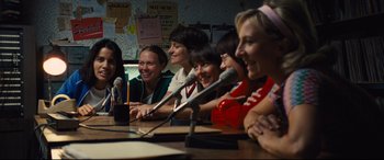 Movie still from “Battle of the Sexes” (2017), directed by Valerie Faris – A group of people sitting at a table with microphones; Medium shot, Over the shoulder angle