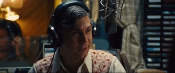 Movie still from “Battle of the Sexes” (2017), directed by Valerie Faris – A man wearing headphones in front of a microphone; Close Up shot, Over the shoulder angle