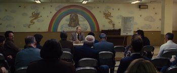 Movie still from “Battle of the Sexes” (2017), directed by Valerie Faris – A group of people sitting in front of a wall with a rainbow; Wide shot, High angle