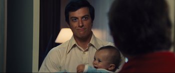 Movie still from “Battle of the Sexes” (2017), directed by Valerie Faris – A man holding a baby in his arms and smiling; Close Up shot, Over the shoulder angle