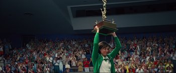 Movie still from “Battle of the Sexes” (2017), directed by Valerie Faris – A woman holding up a trophy in front of an audience; Medium shot, Low angle