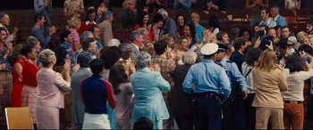 Movie still from “Battle of the Sexes” (2017), directed by Valerie Faris – A group of people standing in front of an audience; Wide shot, High angle