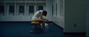 Movie still from “Battle of the Sexes” (2017), directed by Valerie Faris – A woman sitting on top of a bench in a locker room; Wide shot, High angle