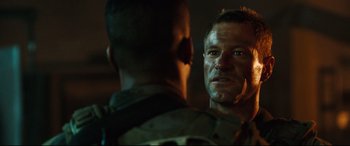 A man in a military uniform looking at another man in fatigues