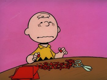 Movie still from “Be My Valentine, Charlie Brown” (1975), directed by Phil Roman – A charlie brown cartoon character sitting at a table with scissors; Close Up shot, High angle