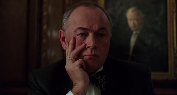 Movie still from “Bean” (1997), directed by Mel Smith – A man in a suit and tie with his hand to his face; Close Up shot, Low angle