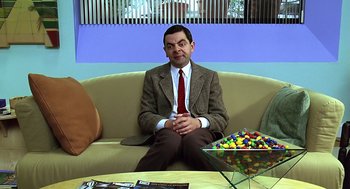 Movie still from “Bean” (1997), directed by Mel Smith – A man sitting on top of a couch in a room; Medium shot, High angle