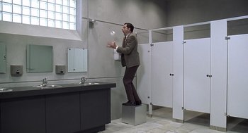 Movie still from “Bean” (1997), directed by Mel Smith – A man standing on top of a box in a bathroom; Wide shot, Low angle