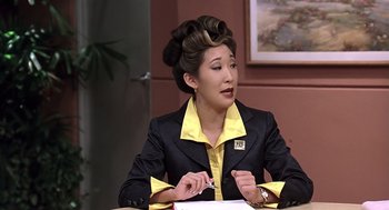 Movie still from “Bean” (1997), directed by Mel Smith – A woman sitting at a table in front of papers; Medium shot, Over the shoulder angle