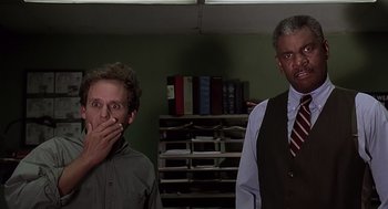 Movie still from “Bean” (1997), directed by Mel Smith – Two men standing next to each other in a room; Medium shot, Low angle