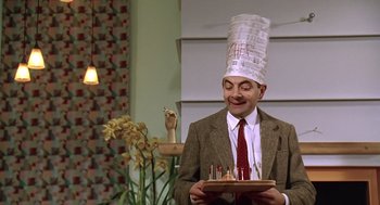 Movie still from “Bean” (1997), directed by Mel Smith – A man wearing a hat and holding a tray of candles; Medium shot, Low angle