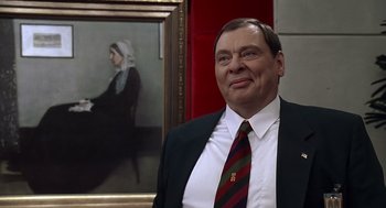 Movie still from “Bean” (1997), directed by Mel Smith – A man wearing a suit and tie standing in front of a painting; Close Up shot, Over the shoulder angle