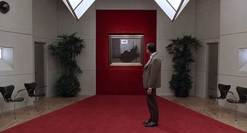Movie still from “Bean” (1997), directed by Mel Smith – A man standing in front of a painting on a red carpet; Wide shot, High angle