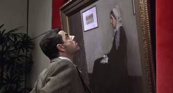 Movie still from “Bean” (1997), directed by Mel Smith – A man standing in front of a painting of an old woman; Close Up shot, Low angle