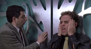 Movie still from “Bean” (1997), directed by Mel Smith – Two men in suits and ties one of them is holding his hands to his ears; Close Up shot, Over the shoulder angle