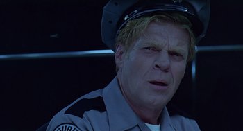 Movie still from “Bean” (1997), directed by Mel Smith – A man in a police officer's uniform is sitting in a car; Close Up shot, Low angle