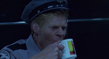 Movie still from “Bean” (1997), directed by Mel Smith – A man in a police uniform drinking from a mug; Close Up shot, Low angle