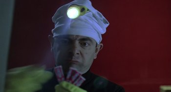 Movie still from “Bean” (1997), directed by Mel Smith – A man wearing a white hat and holding a bunch of cards; Close Up shot, Low angle