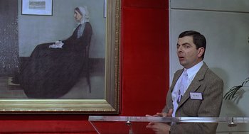 Movie still from “Bean” (1997), directed by Mel Smith – A man standing in front of a painting of a woman; Medium shot, Over the shoulder angle