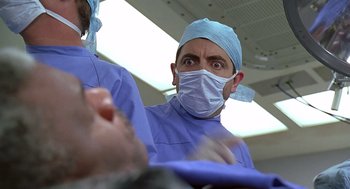 Movie still from “Bean” (1997), directed by Mel Smith – A man wearing a surgical mask and a surgical gown; Close Up shot, Low angle