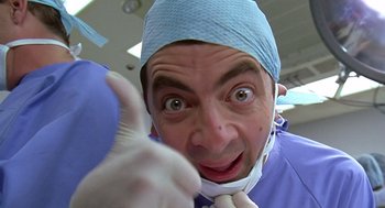 Movie still from “Bean” (1997), directed by Mel Smith – A man wearing a surgical mask and a blue hat; Close Up shot, Low angle