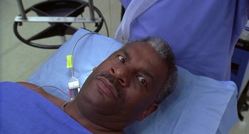 Movie still from “Bean” (1997), directed by Mel Smith – A man laying in a hospital bed looking at the camera; Close Up shot, High angle
