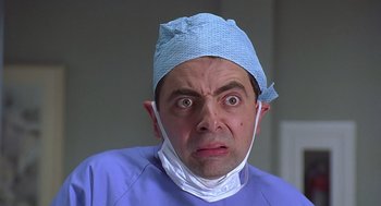 Movie still from “Bean” (1997), directed by Mel Smith – A man wearing a surgical mask and a blue scrub suit; Close Up shot, Low angle