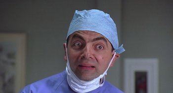 Movie still from “Bean” (1997), directed by Mel Smith – A man wearing a surgical mask and a surgical gown; Close Up shot, Low angle