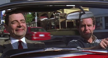 Movie still from “Bean” (1997), directed by Mel Smith – Two men in a red car with an umbrella; Medium shot, Over the shoulder angle