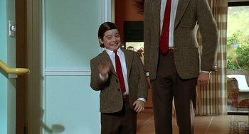 Movie still from “Bean” (1997), directed by Mel Smith – A young boy wearing a suit and tie waving; Medium shot, Over the shoulder angle
