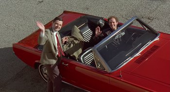 A man and a woman in a red car waving