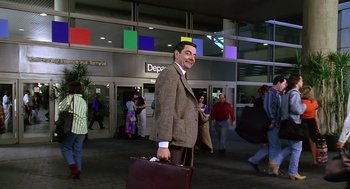 Movie still from “Bean” (1997), directed by Mel Smith – A man in a suit and tie holding a briefcase in an airport; Wide shot, Low angle