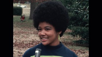 Movie still from “Summer of Soul” (2022), directed by Sanjib Gogoi – A young woman with a large black afro is smiling; Close Up shot, High angle