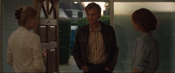 Movie still from “Beast” (2017), directed by Michael Pearce – A man standing in front of a door wearing a brown jacket; Medium shot, Over the shoulder angle