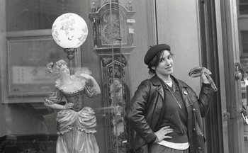 Movie still from “Beastie Boys Story” (2020), directed by Spike Jonze – A black and white photo of a woman standing in front of a clock; Medium shot, Low angle