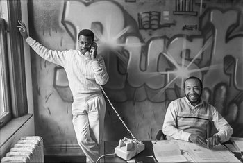 Movie still from “Beastie Boys Story” (2020), directed by Spike Jonze – A man on the phone next to another man in front of a graffiti wall; Medium shot, Low angle