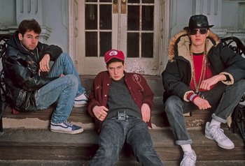 Movie still from “Beastie Boys Story” (2020), directed by Spike Jonze – A group of young men sitting on the steps of a building; Medium shot, Low angle